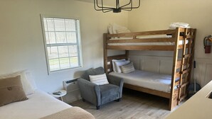 Ein Zimmer mit Etagenbetten, einem grauen Sessel, einem kleinen Tisch und einer Heizung.