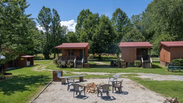 Un terrain de camping doté de cabanes en bois, d’un foyer et de coins salon extérieurs.