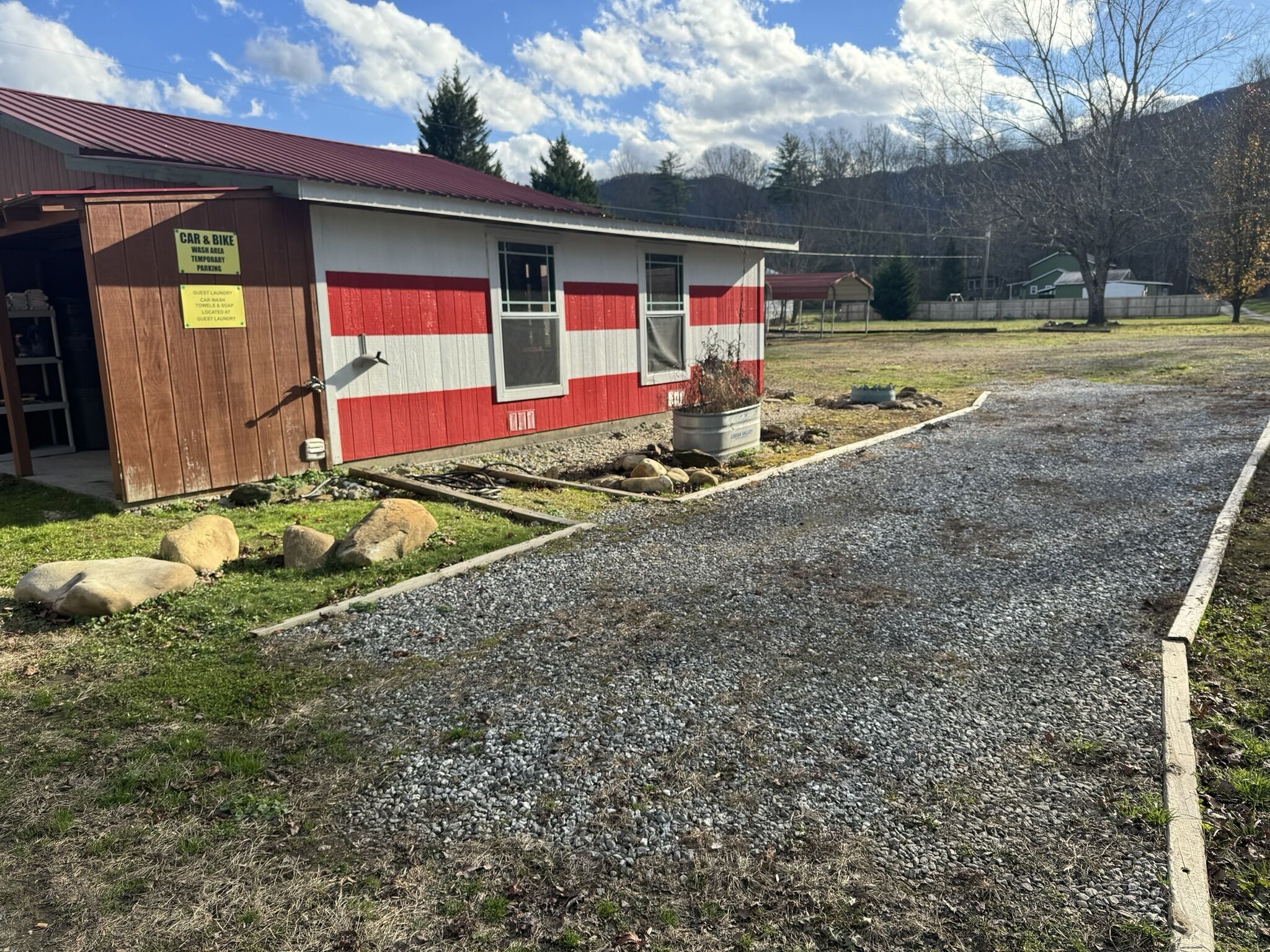A small building with a red and white exterior, a gravel driveway, and a sign indicating car and bike wash area and temporary parking.