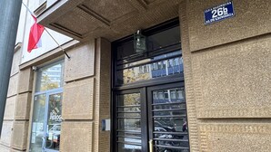 Fachada de edificio con un amplio ventanal, una puerta con manija metálica y un cartel que indica una ubicación en Krowdorz.