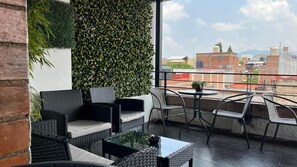 Una terrassa al terrat amb mobles de vimet, una taula de vidre i vista a edificis.