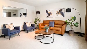 A living room with a brown sofa, two blue armchairs, a coffee table, and a floor lamp. - Modern Comforts Downtown Living within walking distance to all the conveniences  (Yorkton)