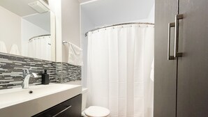 A modern bathroom with a white sink, a mirror, a toilet, and a shower curtain. - Modern Comforts Downtown Living within walking distance to all the conveniences  (Yorkton)