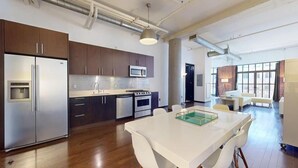 A modern kitchen with stainless steel appliances, a large island, and a dining area with a white table and chairs.