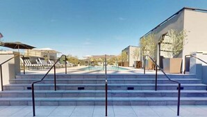 A pool area with steps leading down to the water, a covered seating area, and a building with a flat roof.