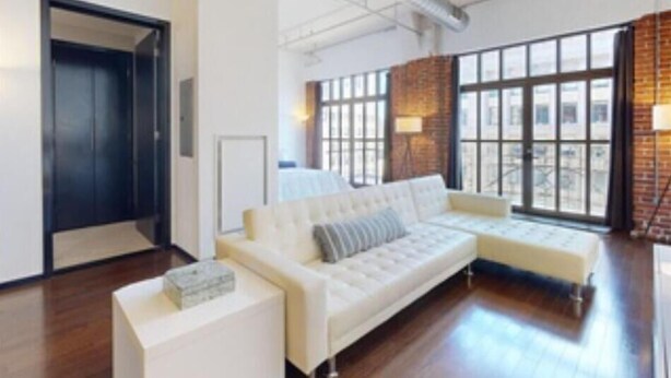 A modern living room with a white sofa, a small white table, and a large window with a view of the city.