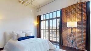 A modern bedroom with a large bed, a brick wall, and a floor lamp.