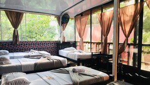 Een kamer met drie bedden, elk voorzien van een kussen en een deken, en een ventilator aan de muur.