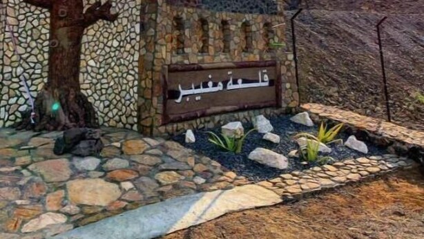 A stone wall with Arabic script, a flag, and a tree. - Fort Mughaibar Resort (Hatta)