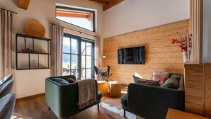 Un salón acogedor con techo de madera, un ventanal amplio, un televisor de pantalla plana y decoración rústica.