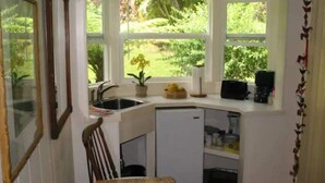 A compact kitchen with a window overlooking a garden, a sink, and a small refrigerator.