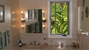 A bathroom with a large mirror, a window with a view of greenery, and a sink with multiple faucets.