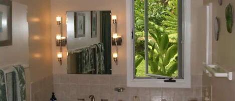 A bathroom with a large mirror, a window with a view of greenery, and a sink with multiple faucets.
