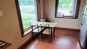 A small kitchen with a dining table and chairs, large windows, and a refrigerator.