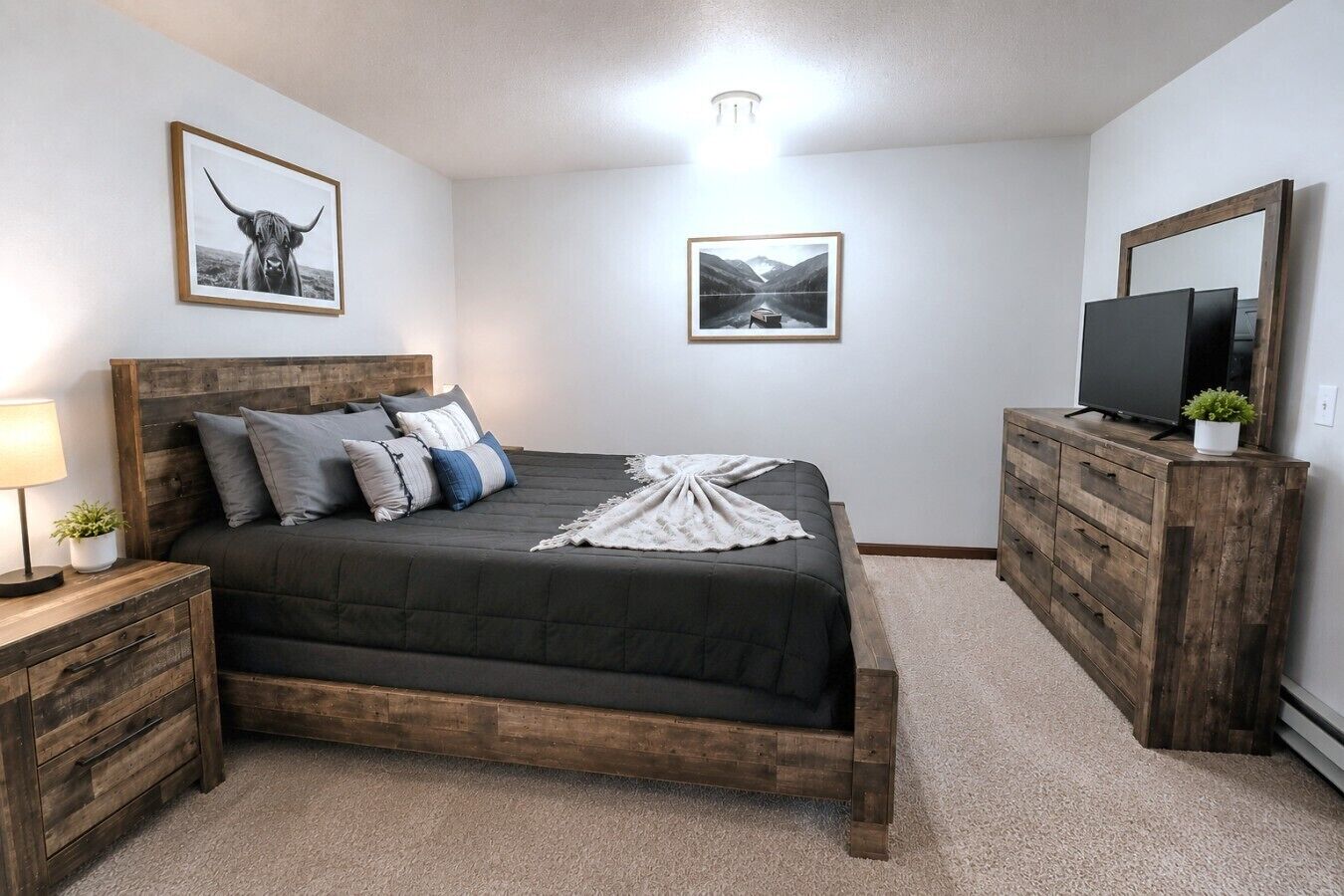 Une chambre à coucher avec un lit en bois, une table de chevet avec une lampe, une commode et deux tableaux encadrés accrochés au mur.