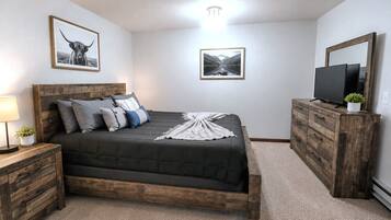 Une chambre à coucher avec un lit en bois, une table de chevet avec une lampe, une commode et deux tableaux encadrés accrochés au mur.