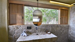 A bathroom with a stone wall, wooden window shutters, and a stone sink with towels and toiletries.