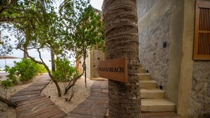 Un sentier en bois menant à une plage, un palmier et un panneau indiquant « PLAYA BEACH ».