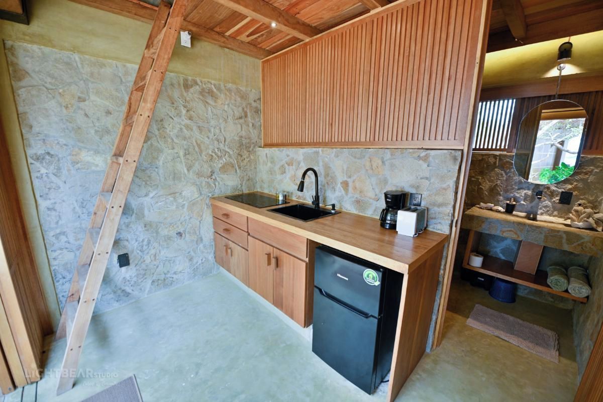 Una cocina compacta con pared de piedra, armarios de madera, un refrigerador negro y un lavamanos.