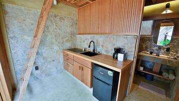 Una cocina compacta con pared de piedra, armarios de madera, un refrigerador negro y un lavamanos.