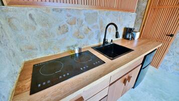 A kitchen with a stone wall, wooden cabinets, a black sink, and a built-in induction cooktop.