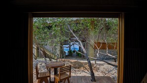 Une terrasse en bois avec une table et des chaises, qui mène à un escalier en pierre et offre une vue sur la mer.