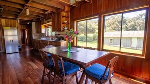 A wooden interior with a dining table, chairs, a kitchen area, and large windows. - Mountain Wonders Chalet: Perfect to enjoy nature (Provincia de Puntarenas)