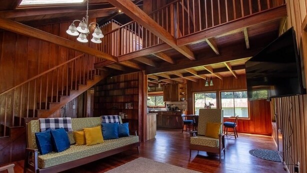 A spacious living area with a wooden staircase, a sofa with cushions, a dining area, and a kitchen visible through an open door. - Mountain Wonders Chalet: Perfect to enjoy nature (Provincia de Puntarenas)