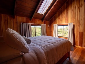 Een kamer met houten vloeren, een bed, grote ramen en een dakraam.