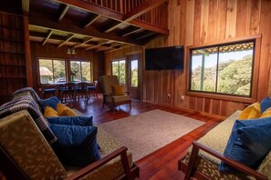 Un intĂ©rieur en bois avec un tĂ©lĂ©viseur, un coin salon et de grandes fenĂȘtres.