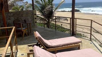 A beachside lounge with wooden loungers, a stone wall, and a view of the ocean.