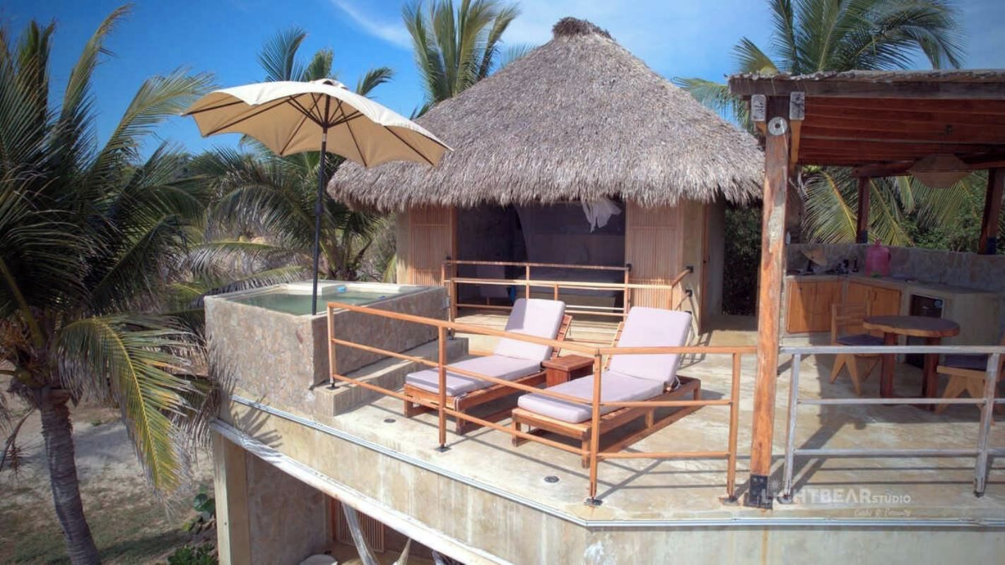 A thatched-roof structure with a pool, lounge chairs, and a wooden deck.