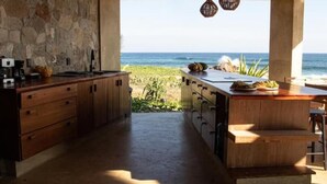 A kitchen with a view of the ocean, wooden cabinets, and a stone wall.