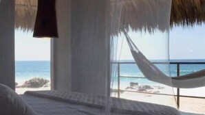 A bed with a mosquito net, a hanging light fixture, and a view of the beach and ocean.