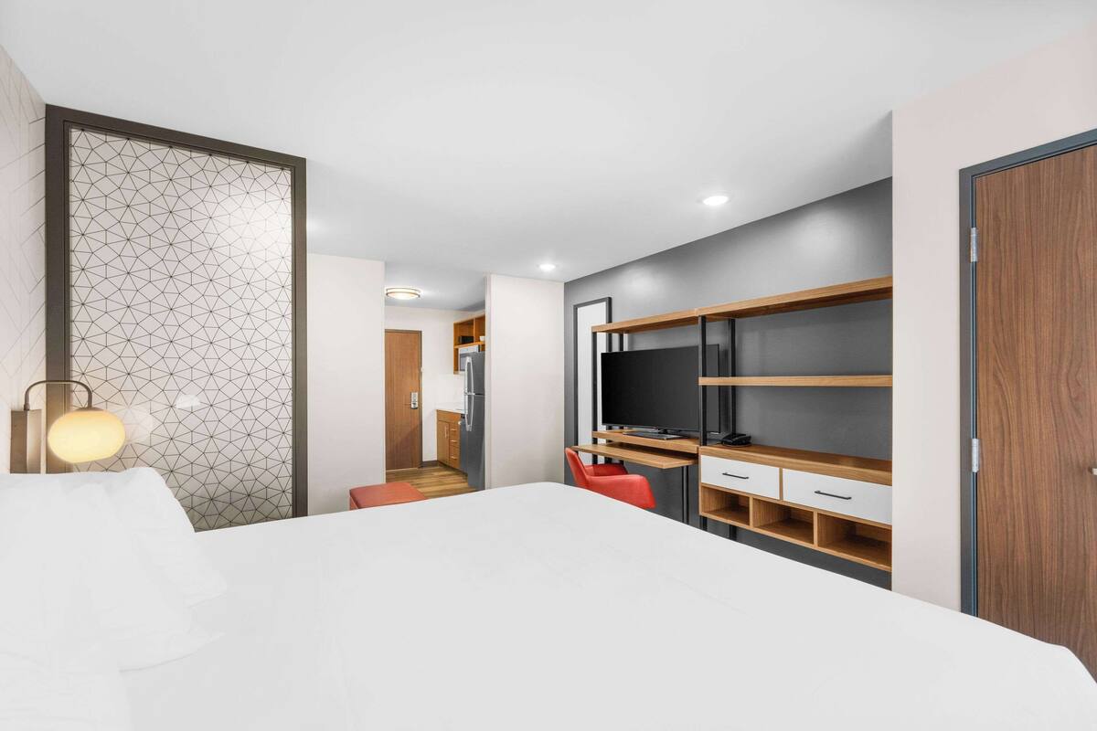 Una habitación de hotel moderna con una cama, un escritorio con computadora, un televisor y un armario.