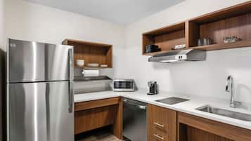 A modern kitchen with a stainless steel refrigerator, microwave, and dishwasher, wooden cabinets, and white countertops.