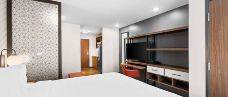 A modern bedroom with a bed, a desk, and a TV.