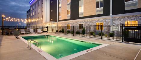A hotel with a swimming pool, outdoor seating, and a stone facade.