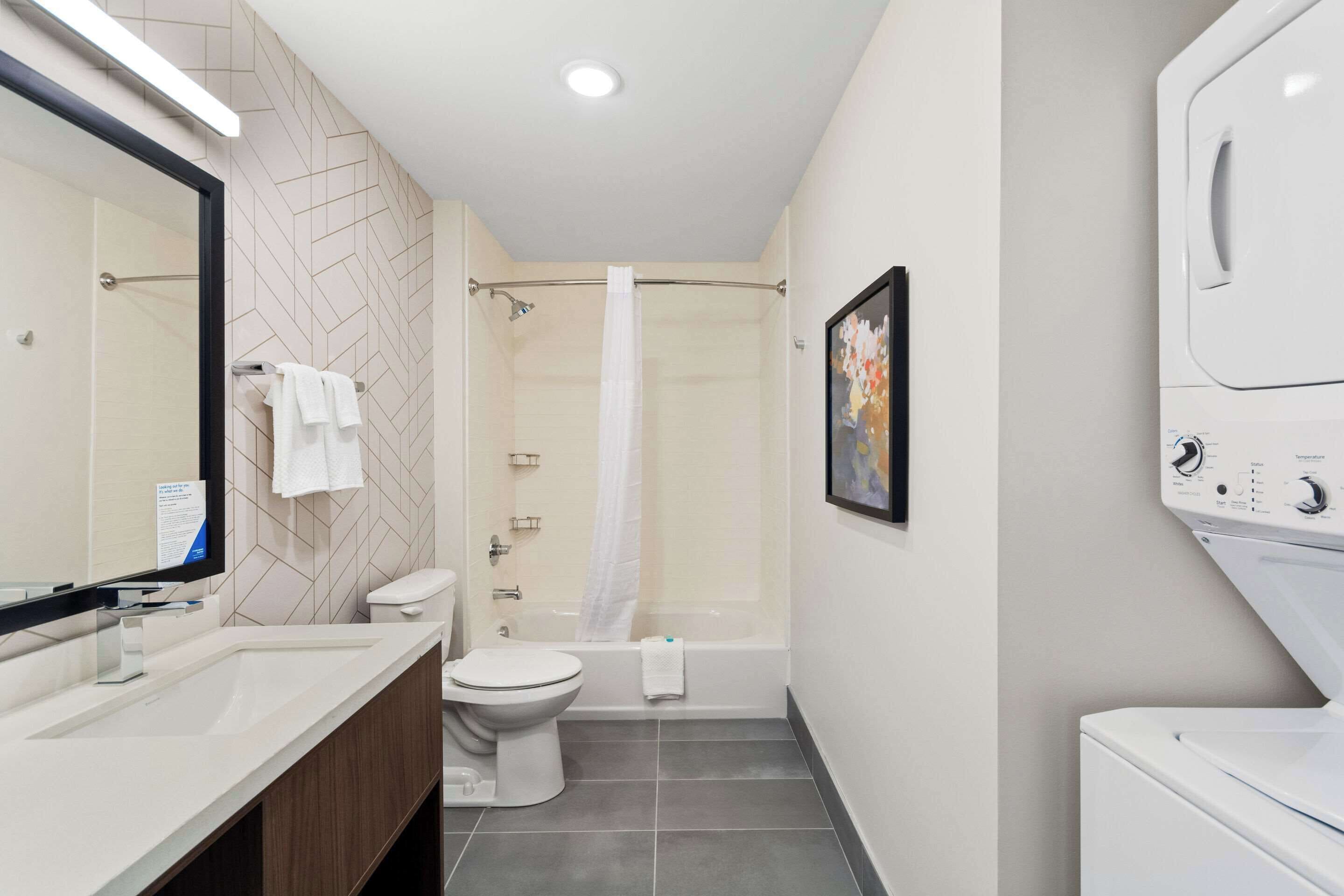 A modern bathroom with a shower, toilet, sink, and a built-in washing machine.