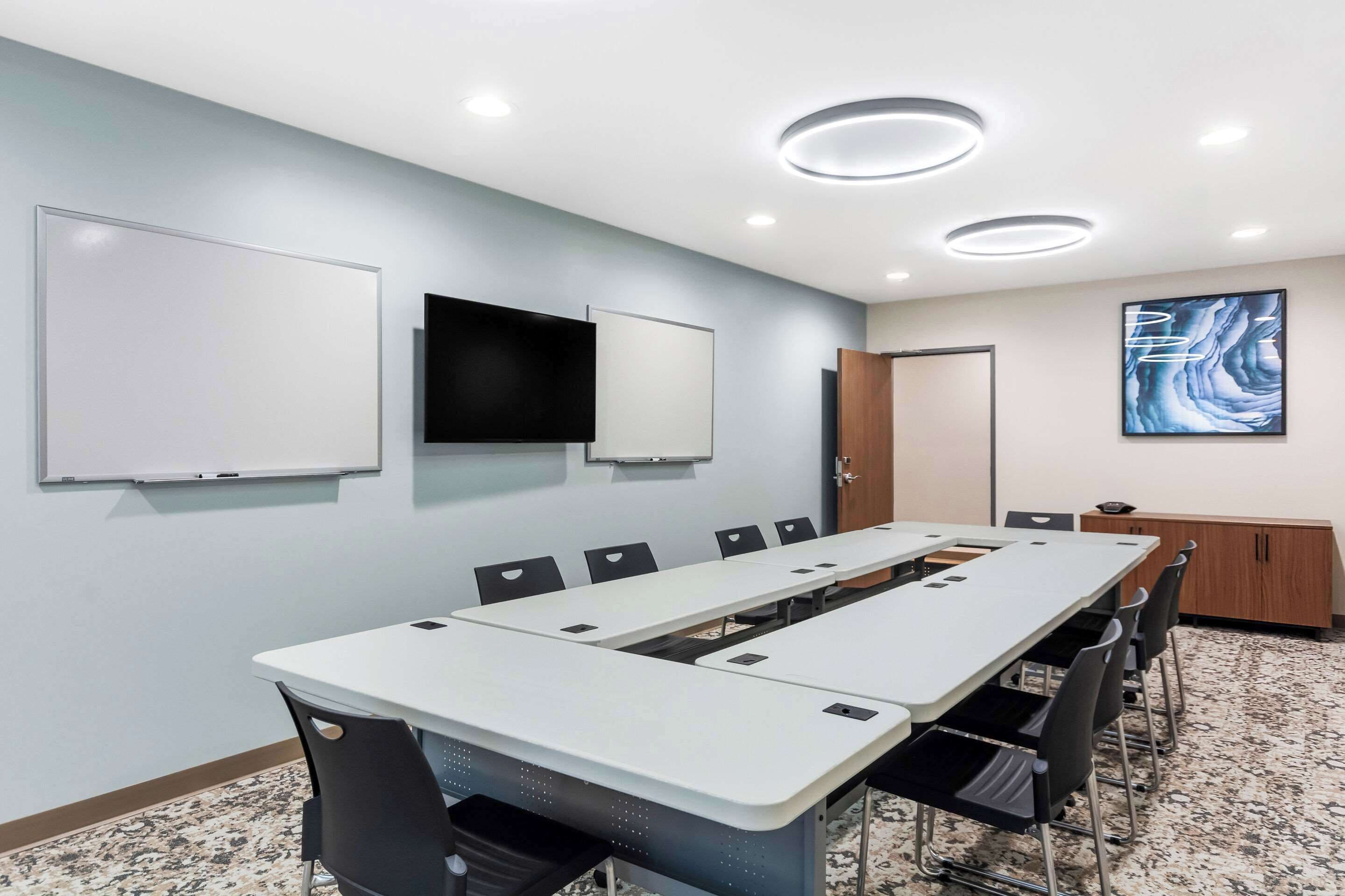 A conference room with a long table, chairs, a whiteboard, a flat-screen TV, and a wooden cabinet.
