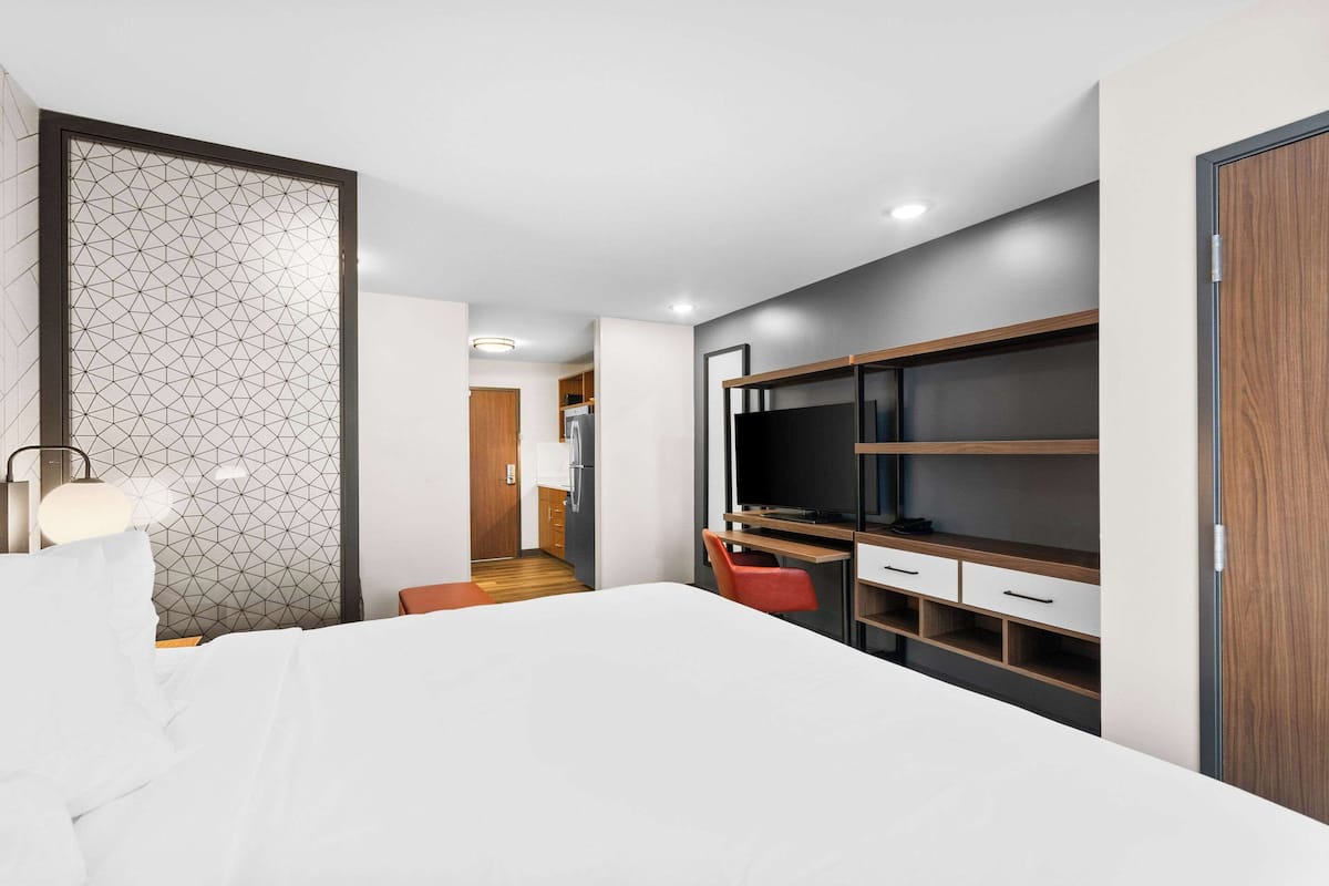 Una habitación de hotel moderna con una cama grande, un escritorio con televisor y un armario.