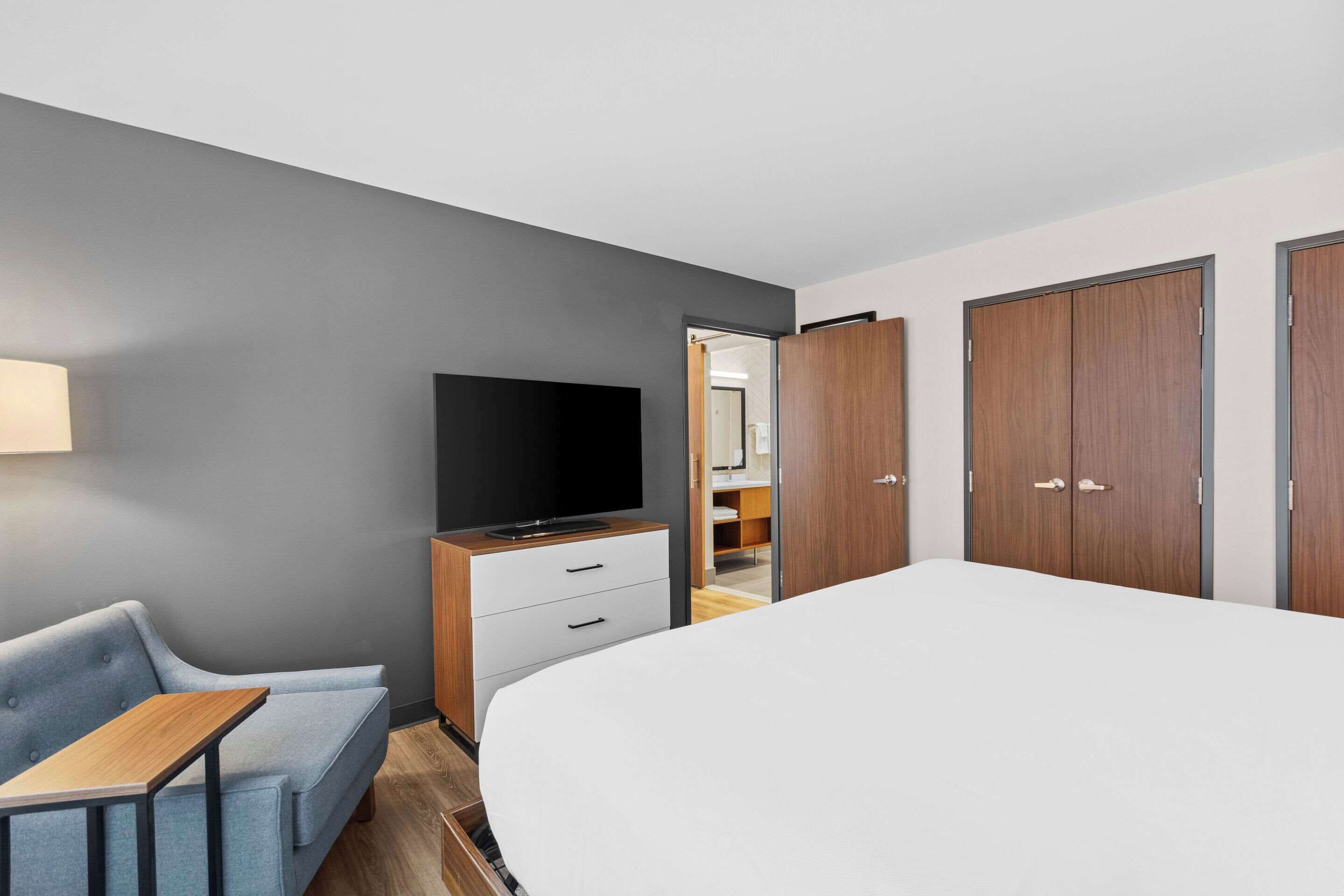 Een moderne hotelkamer met een groot bed, een televisie op een houten dressoir, een bank en een bureau.