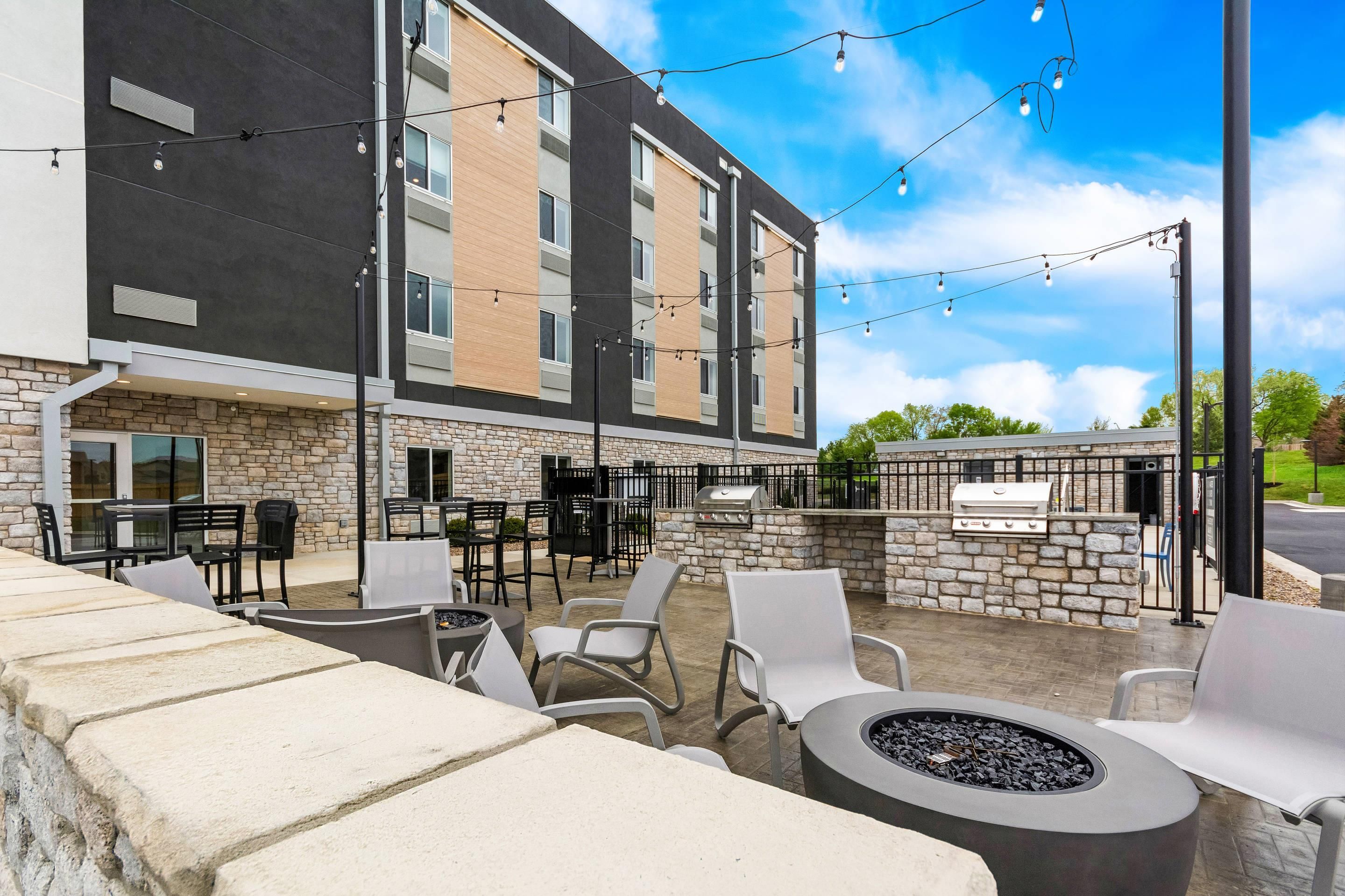 An outdoor patio area with stone seating, tables, and chairs, a fire pit, and a barbecue grill.