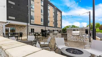 An outdoor patio area with stone seating, tables, and chairs, a fire pit, and a barbecue grill.