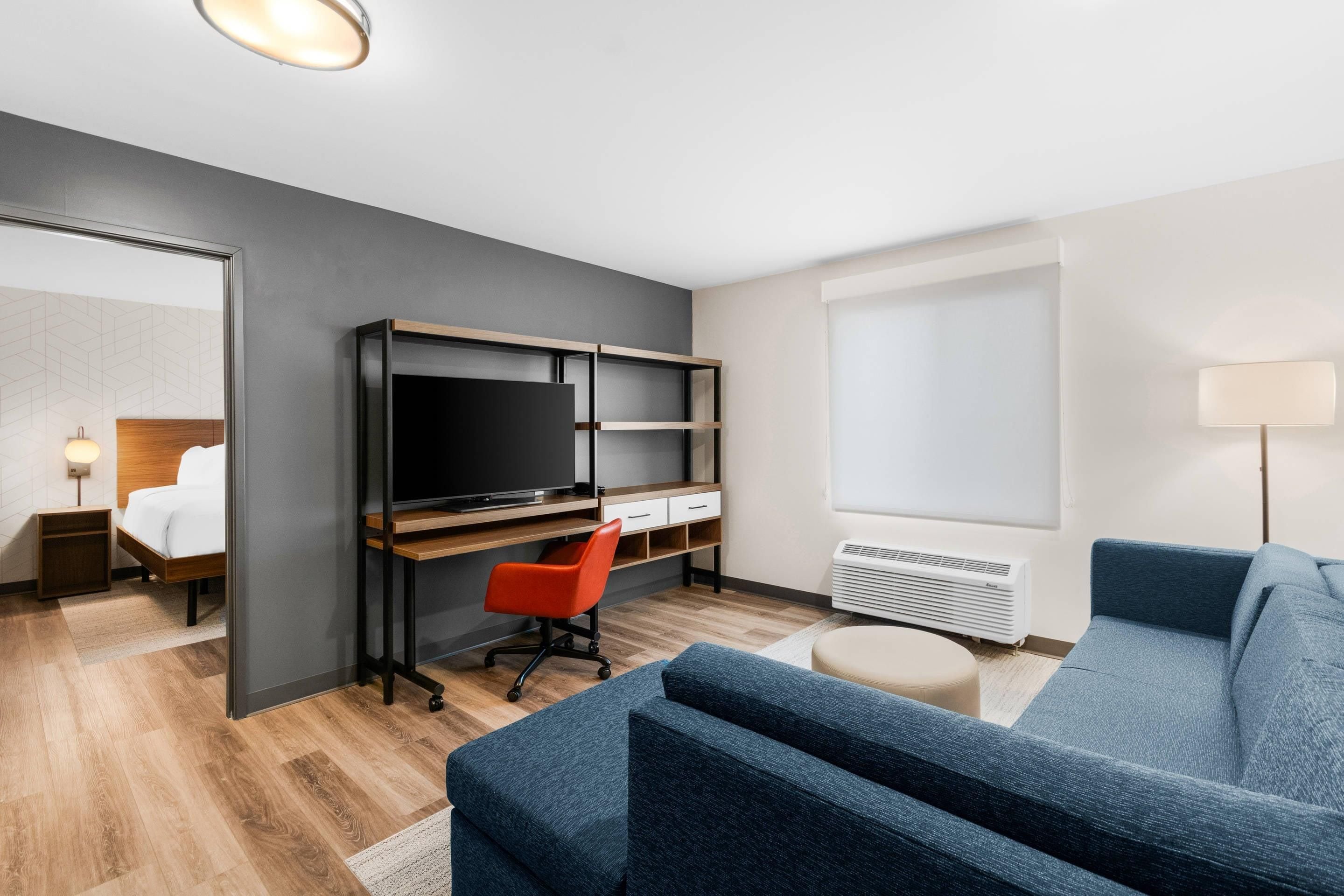 Una camera d'albergo moderna con un letto, una scrivania con televisore, un divano blu e una finestra vista.
