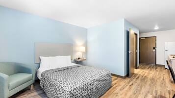 Habitación de hotel con cama, mesita de noche, lámpara, sillón y piso de madera.