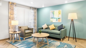 A living room with a sofa, two side tables, a lamp, and a painting on the wall. - Woodspring Suites Bluffdale Salt Lake City (Bluffdale)