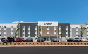 A modern hotel with a flat roof, multiple floors, and a parking lot with several cars. - Woodspring Suites Bluffdale Salt Lake City (Bluffdale)