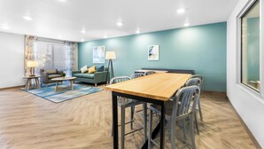 A modern living room with a wooden dining table, grey chairs, a sofa, and a coffee table. - Woodspring Suites Bluffdale Salt Lake City (Bluffdale)