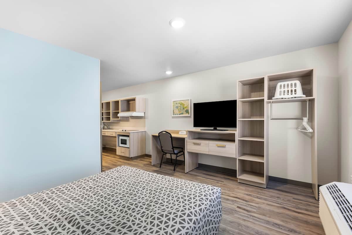 A modern room with a bed, desk, TV, and built-in storage.